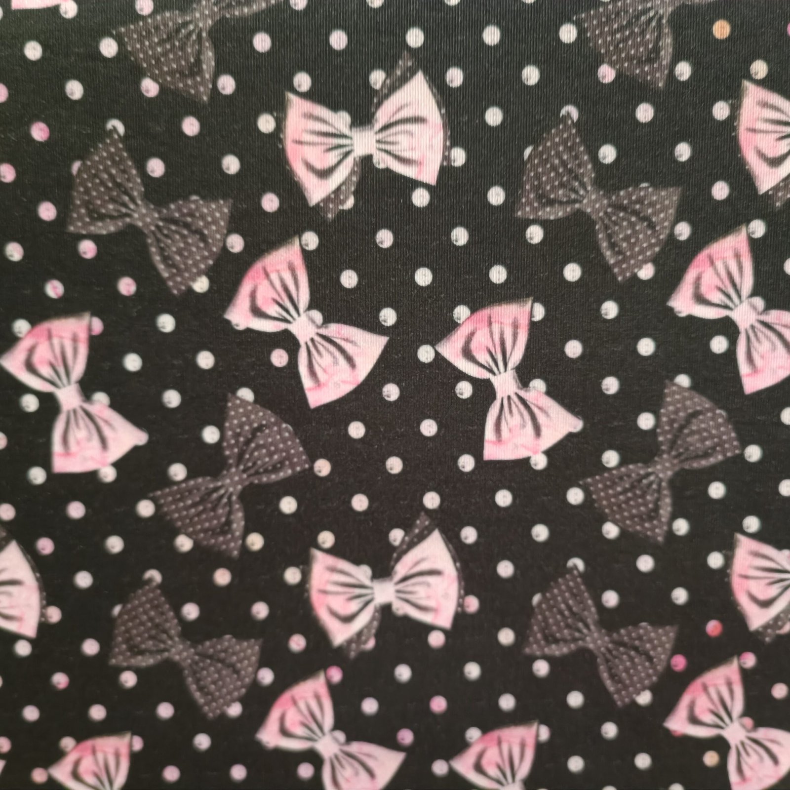 Tecido Microfibra Estampa Digital com laços rosa e laços cinza com poás, sobre fundo preto com poás brancos, da Evelin Tecidos e Aviamentos.