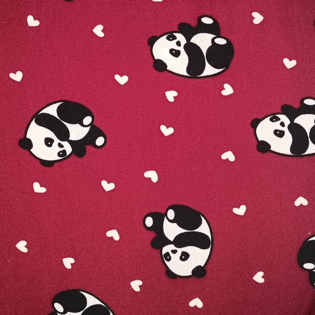 Tecido Suede ST06 com estampa de pandas e corações sobre fundo vermelho, tipo liganete (malha fria), ideal para lingerie divertida e confortável.